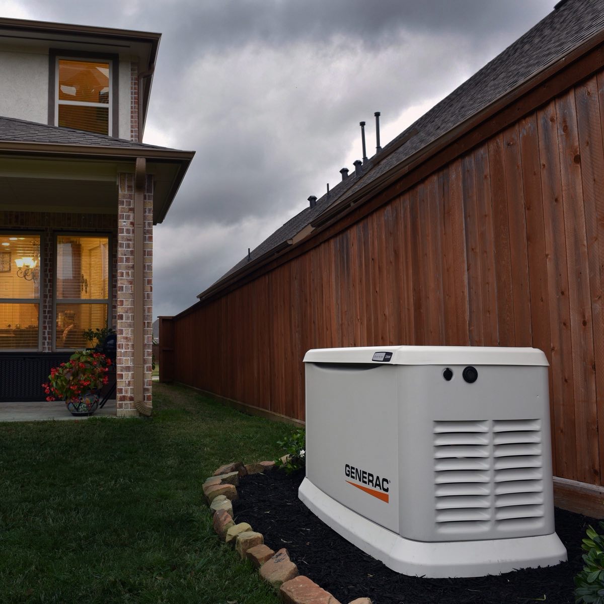 A Generac standby generator installed beside a home, with warm-lit windows under a stormy Oklahoma sky